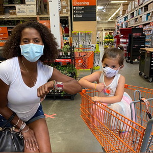 photo of a black woman and a young white girl wearing masks and bumping elbows