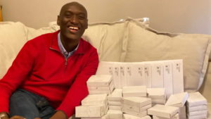 Black man in red sweater sitting on a beige couch beside envelopes and boxes
