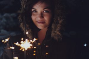 young woman in a fur rimmed parka hood, holding a sparkler